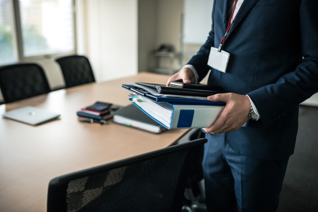 書類とノートパソコンを手に持つビジネスパーソン